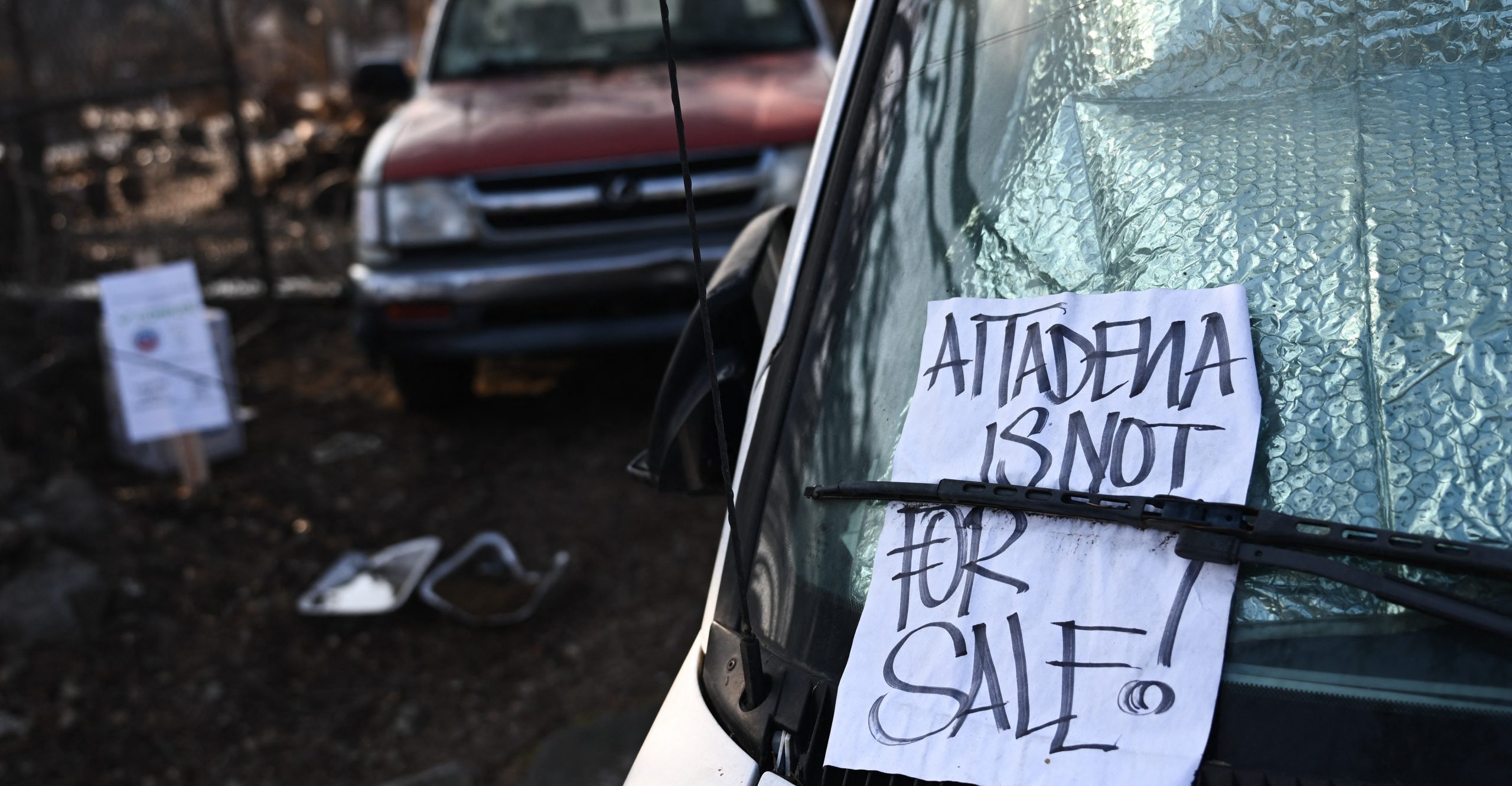 A sign is displayed on a car window reading "Altadena is not for sale" A sign is displayed on a car window reading "Altadena is not for sale"