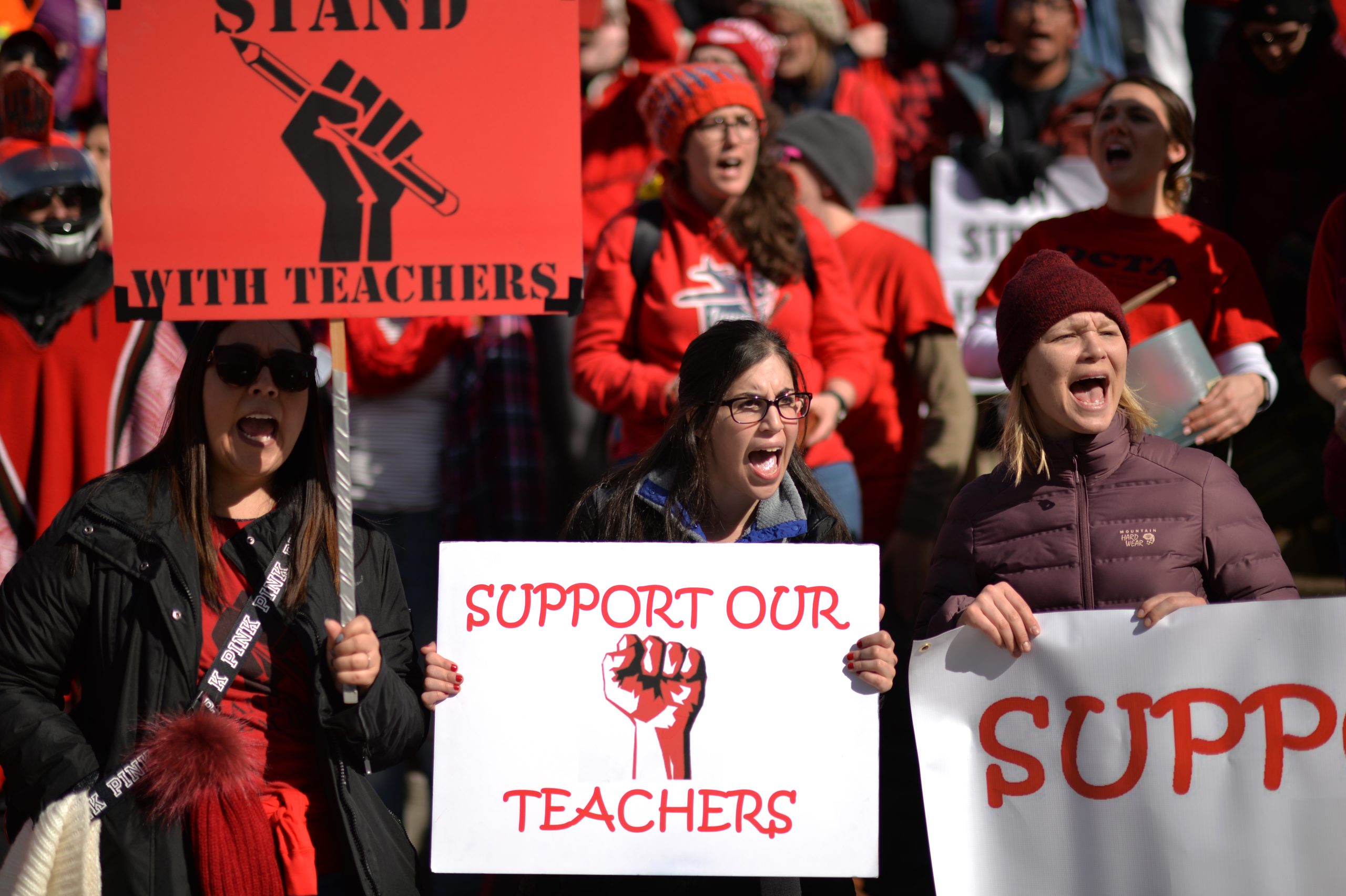 People dressed in red hold signs reading “support our teachers”