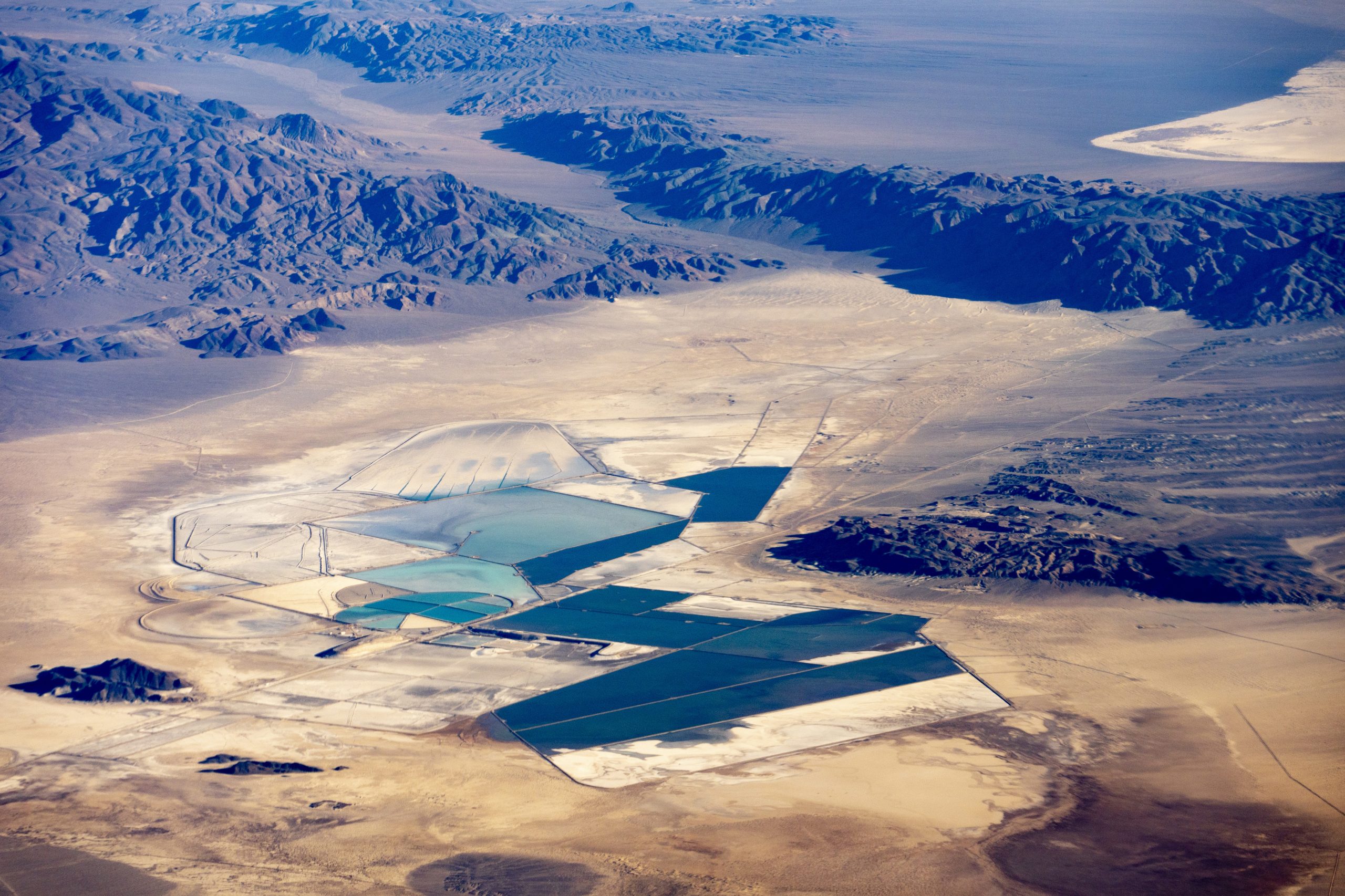 A mine spreads out over an area of desert with water pools nearby and a mountain range in the distance.