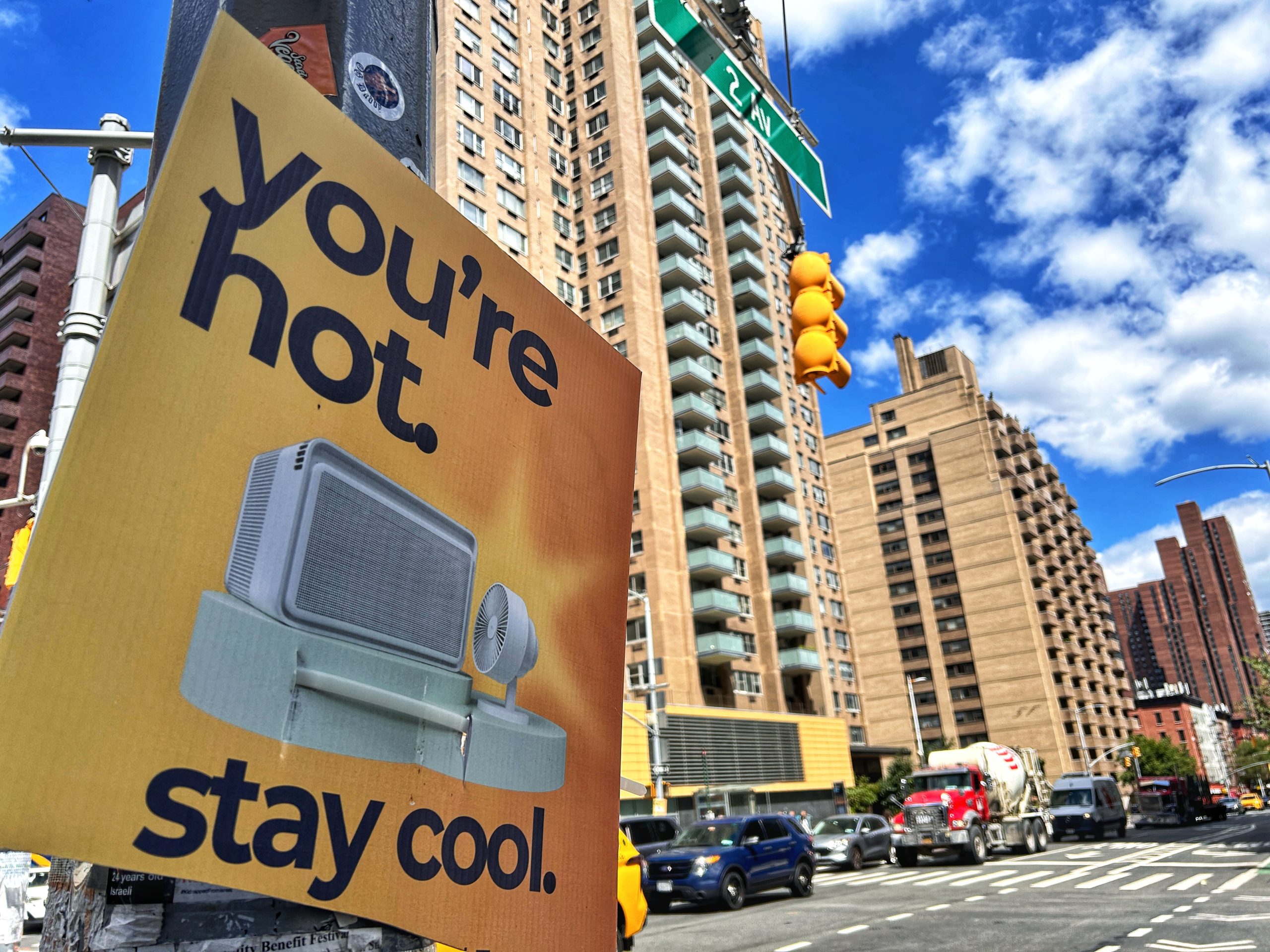 A yellow sign reading “You’re hot, stay cool,” with tall buildings in the background.