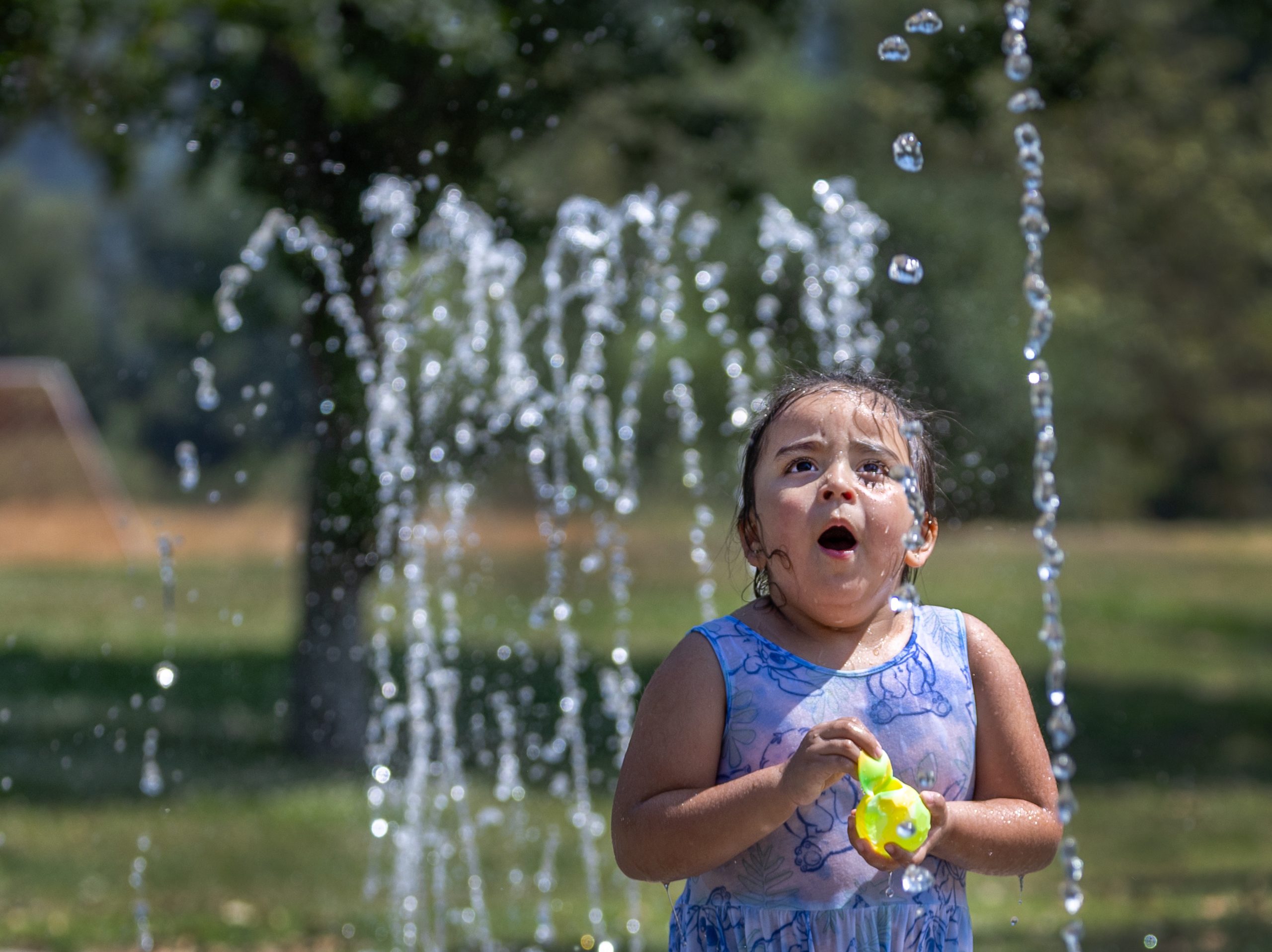 A young girl with dark hair in a purple swimsuit cools off in a water fountain. 