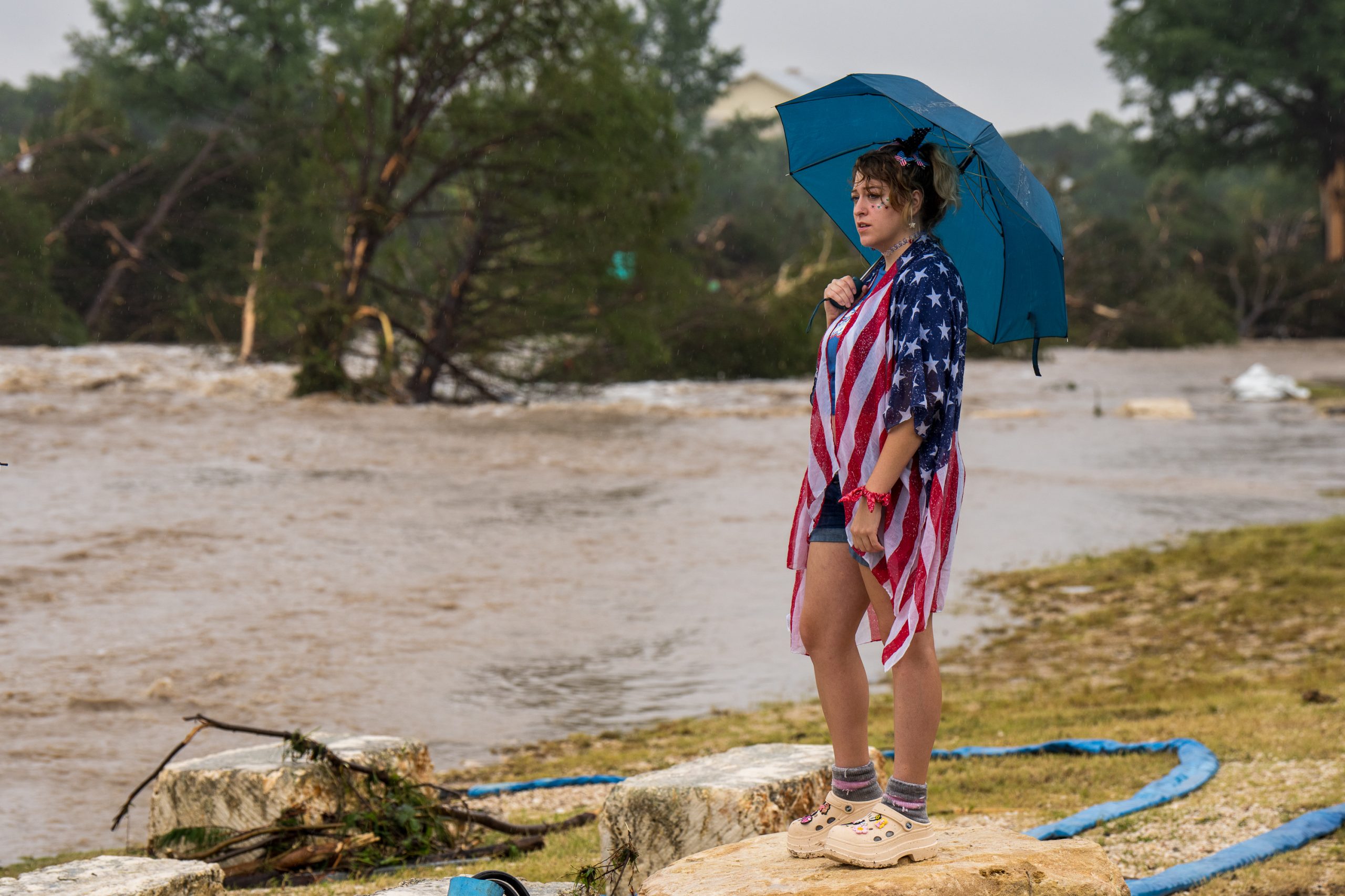 Kerrville resident Leighton Sterling watches flood waters along the Guadalupe River on July 4, 2025. She is wearing a stars and stripped patterned blouse. 