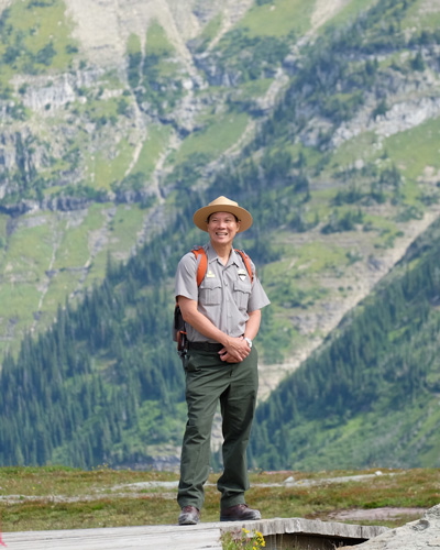 A Park Service employee, an Asian man, dressed in his uniform standing at Glacier National Park
