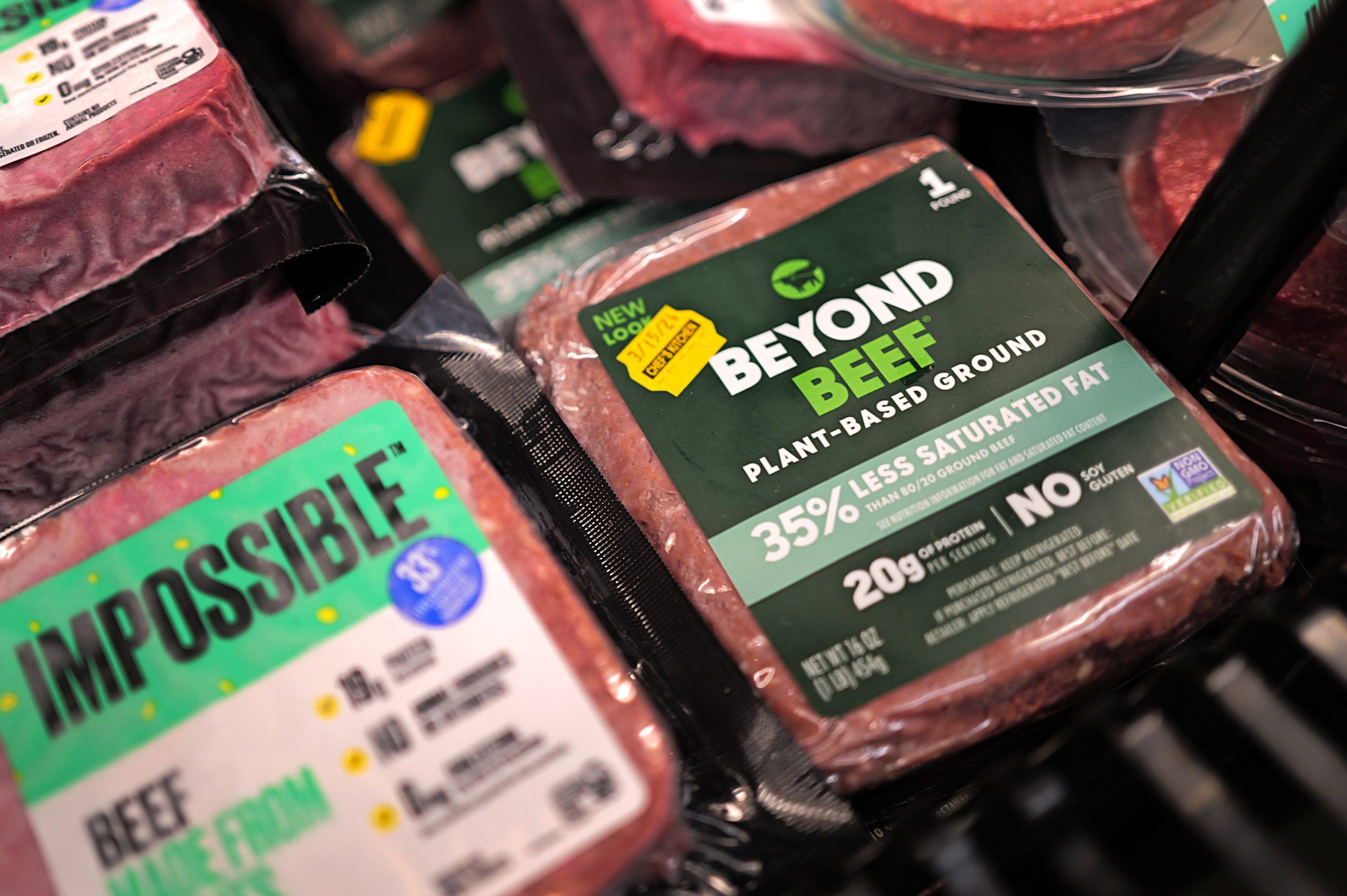 A package of ground Impossible Foods beef sits next to a package of ground Beyond Beef on a supermarket shelf. 