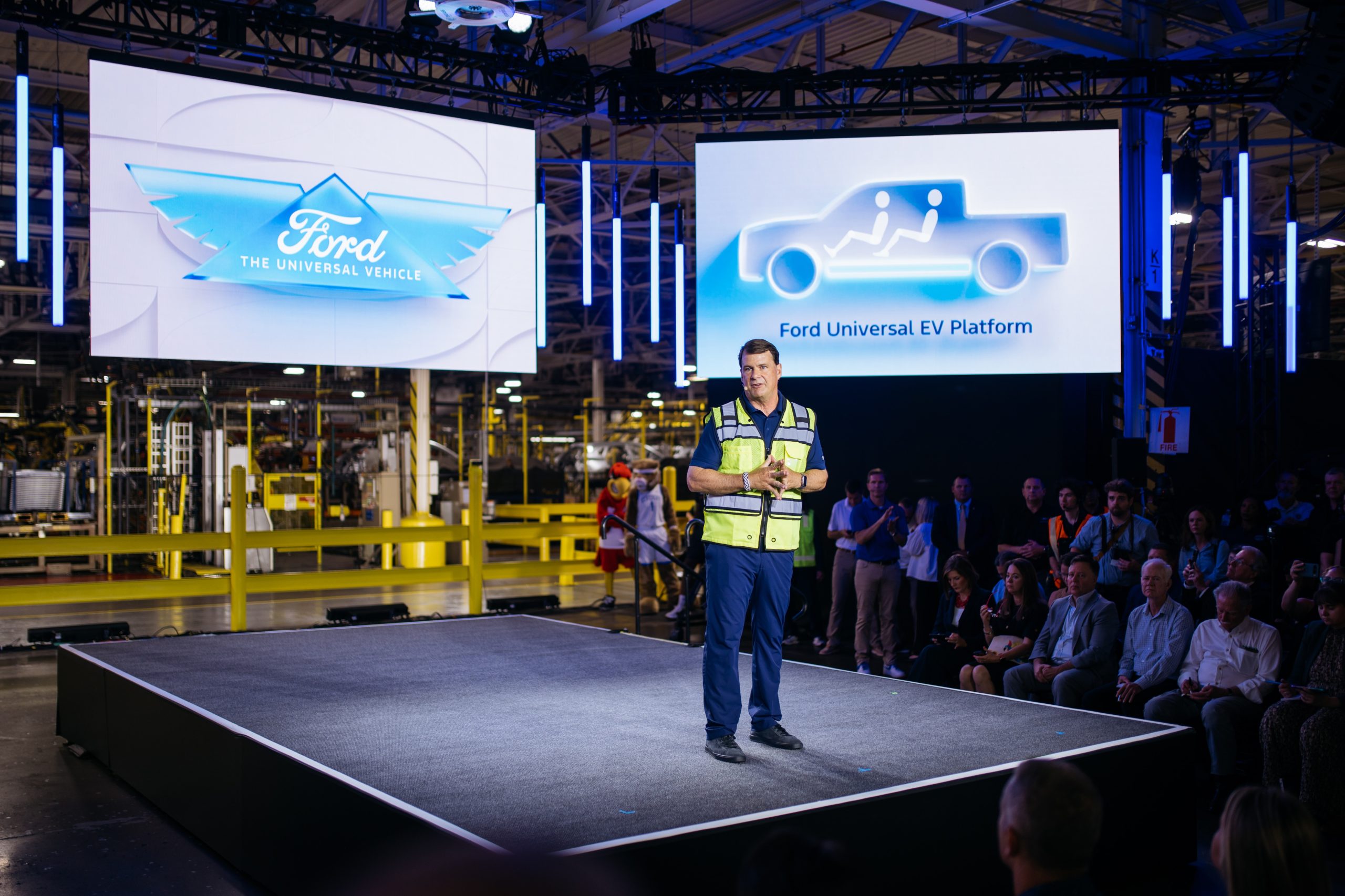 Ford President and CEO Jim Farley stands on a stage in front of two electronic screens.