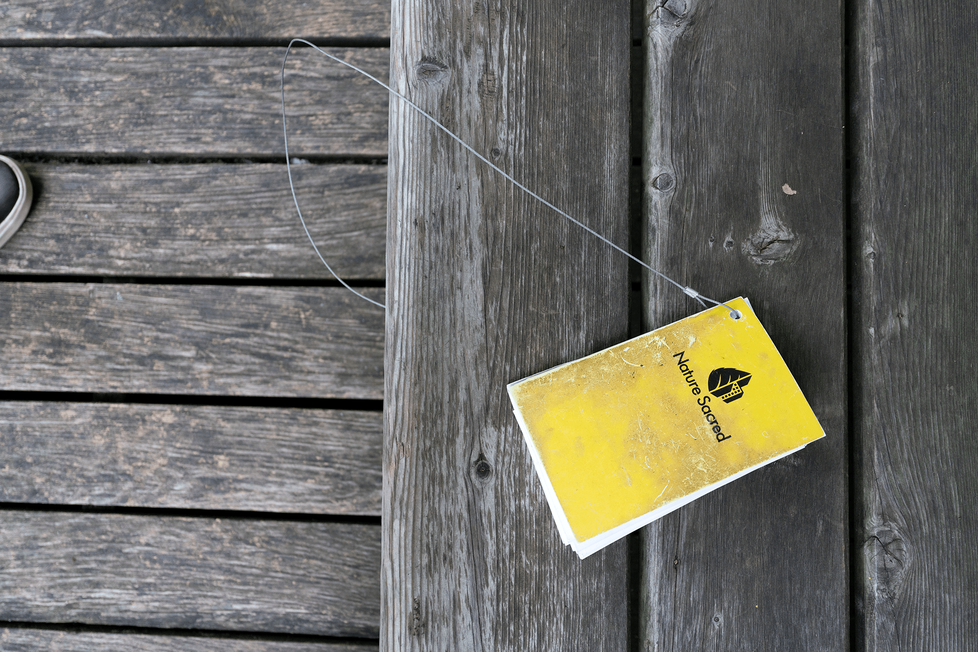 A small yellow notebook, looking weathered, attached to a wire string on wood for people to write in