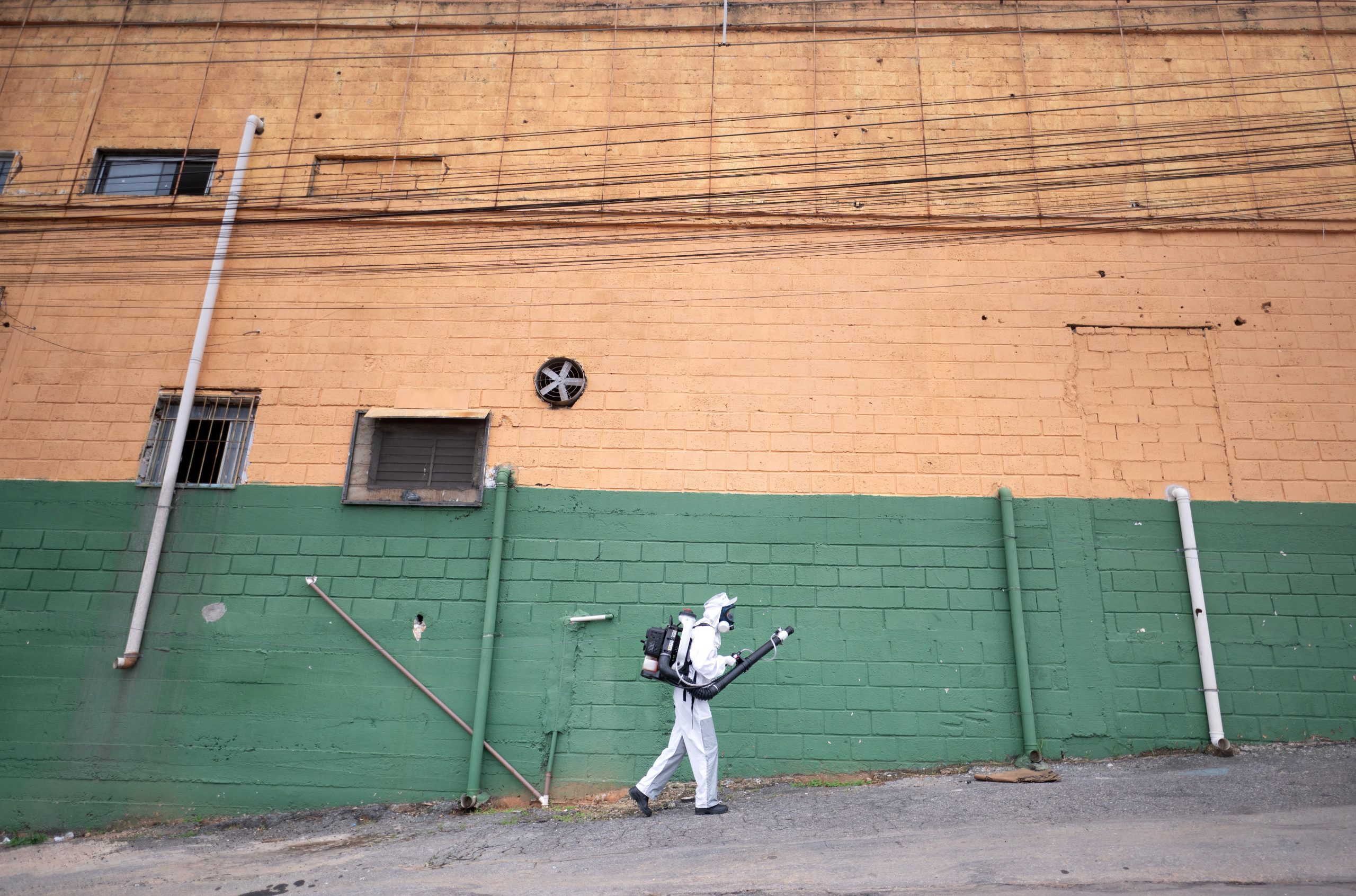 A health worker in white PPE fumigates on a Brazilian street