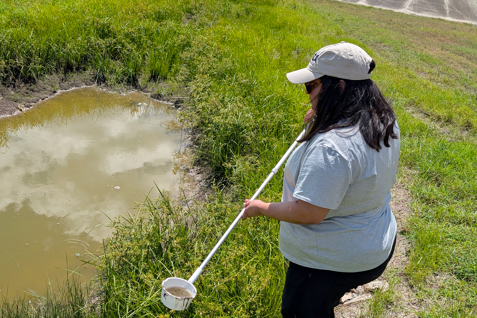 A woman uses a tool to examine water in a roadside ditch