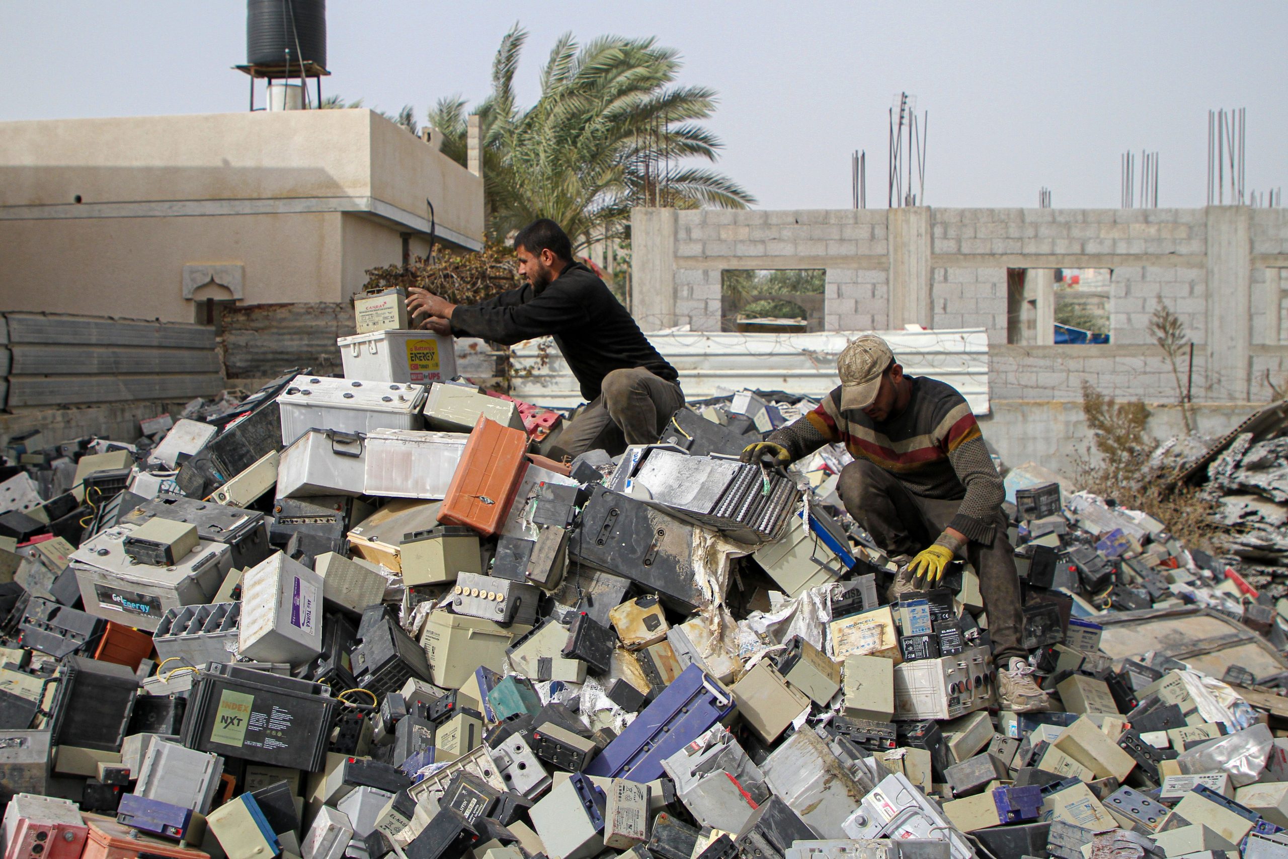 Two workers climb over a large pile of damaged lead-acid batteries in Khan Younis, Gaza, December 2021.