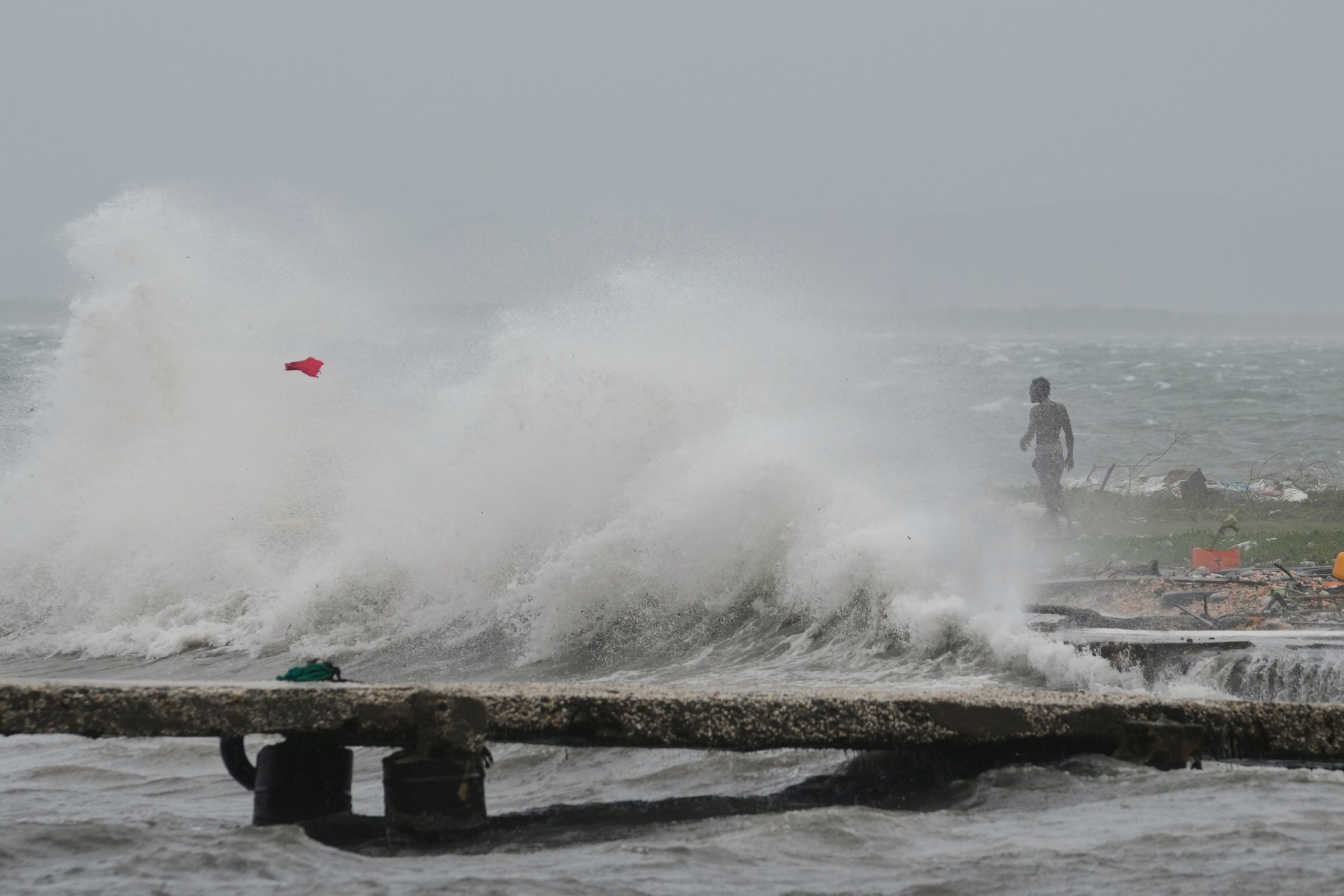 A man is seen in the background at a beach and a wave crashes in anticipation of Hurricane Melissa’s landfall.