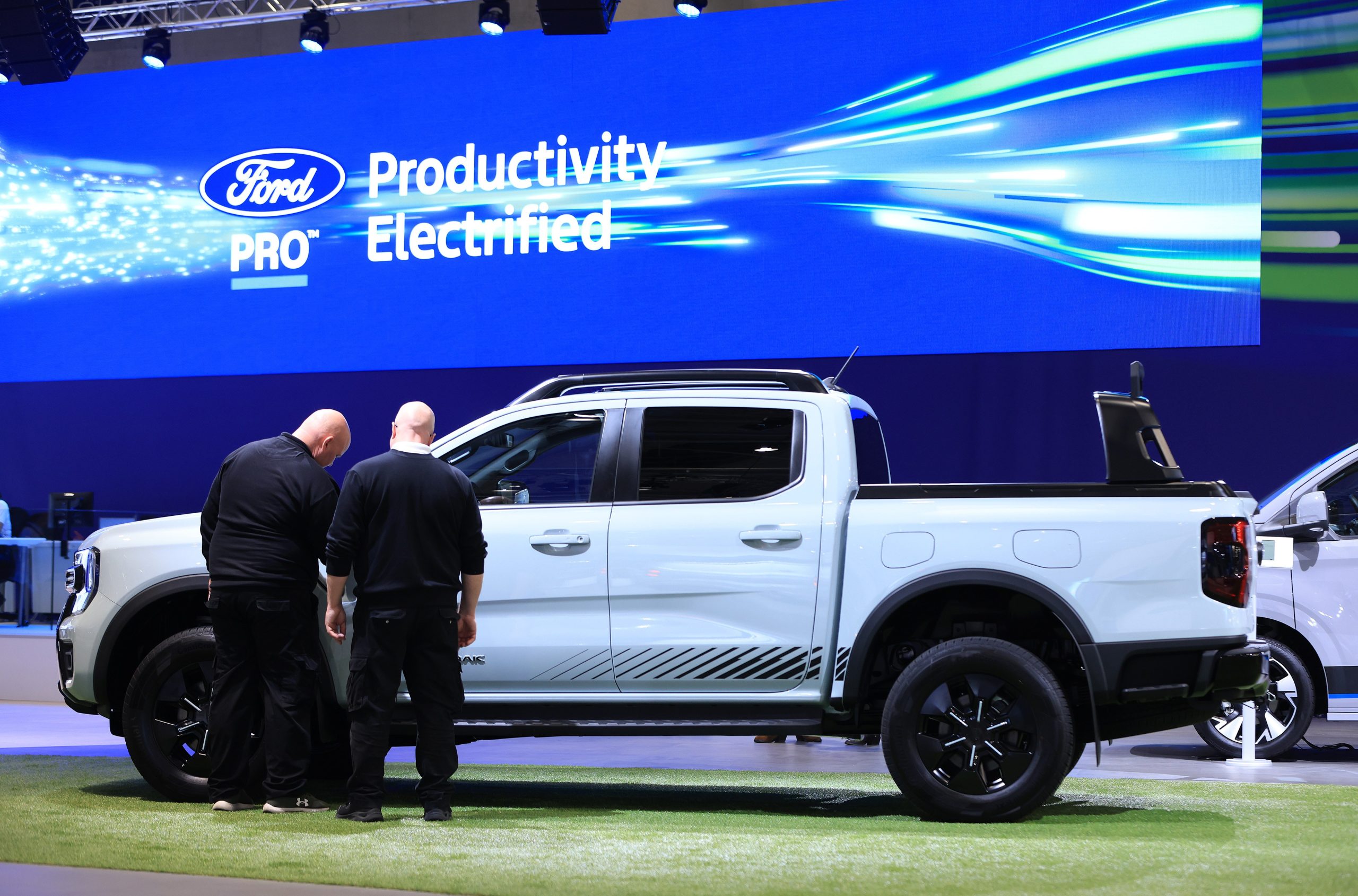 Two men examine a large white Ford truck at a vehicle trade show.